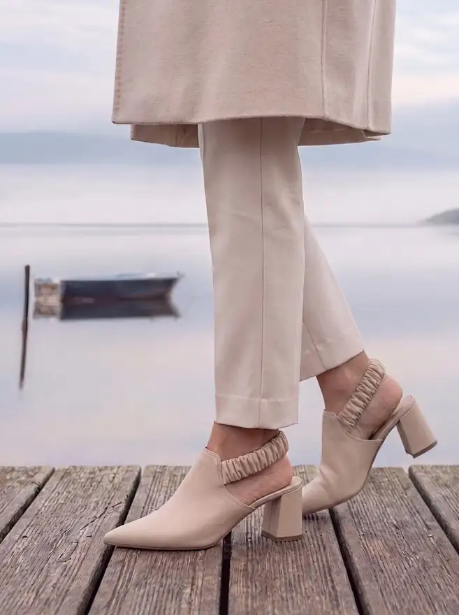 Mascaró campaign image made with Ai: a woman in cream trousers and slingbacks on a wooden jetty by a misty lake