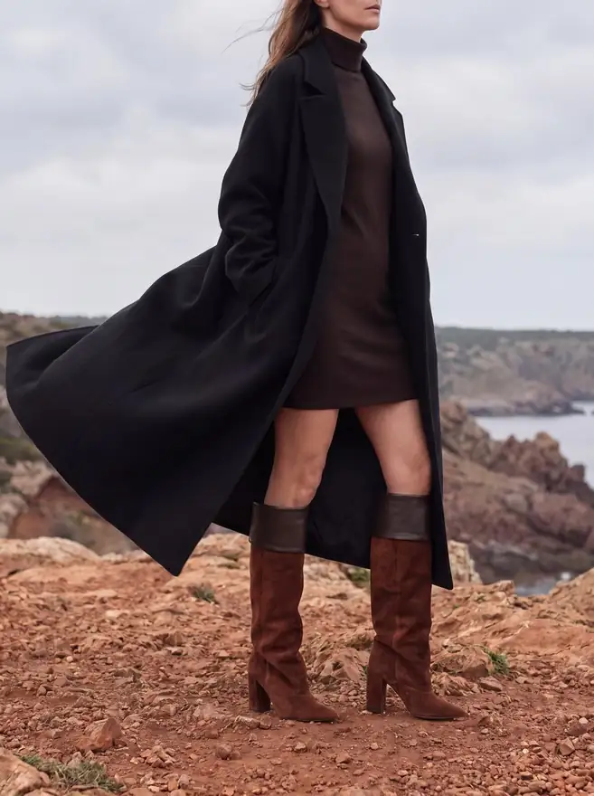 Mascaró campaign image made with Ai: a woman in a long black coat and suede knee boots on a red coastline